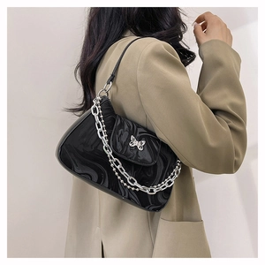 Détail du sac bandoulière noir à texture fluide avec boucle papillon argentée sur costume