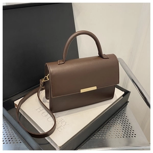 Detail of dark brown leather crossbody bag with minimalist gold metal buckle on a gift box