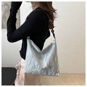 Detail of silver pleated shoulder bag featuring distinctive dark brown wooden bead strap