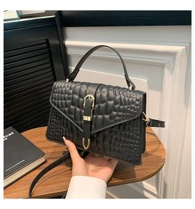 Detail of black crocodile pattern leather handbag with gold metal clasp on a wooden table