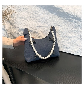 Detail of dark blue denim handbag featuring pearl strap and bow accents