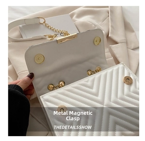 Detail of white quilted handbag showing magnetic gold buckle and sleek metal chain strap