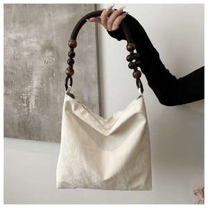 Detail of a beige velvet underarm bag with wooden bead handle and braided cord strap