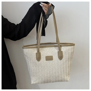 Close-up of large woven straw tote bag with brown leather straps and herringbone texture