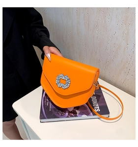 Détail macro du sac bandoulière orange vif avec une boucle scintillante en strass