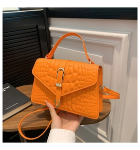 Detail of bright orange handbag with crocodile texture and gold clasp on a cafe table