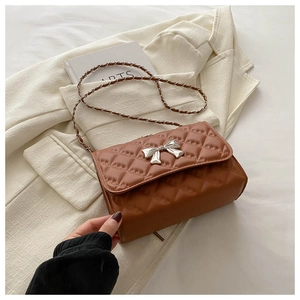 Detailed view of caramel brown quilted leather bag with silver bow accent and chain strap