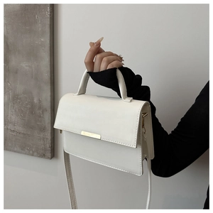 Detailed close-up of white leather handbag with golden metal hardware and top handle