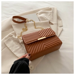Detail of brown V-quilted faux leather crossbody bag with golden metal hardware and chain