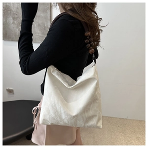Detail of white pleated shoulder bag featuring elegant dark wooden beads on strap