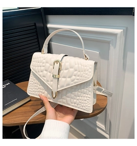 Detail of white crocodile embossed handbag with polished gold buckle and top handle