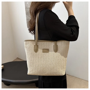 Detail of woven straw tote bag with brown leather straps and square logo patch