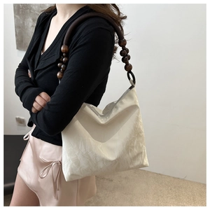 Detail of off-white pleated fabric shoulder bag featuring vintage wooden bead strap