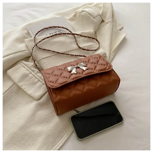 Detail view of brown quilted crossbody bag with silver bow accent next to a phone