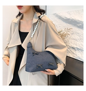 Detailed view of navy denim shoulder bag featuring large white pearls and bow accents