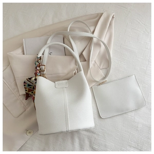 Detail der weißen Eimer-Tasche aus Leder mit Litschimuster und dekorativem Seidenschal