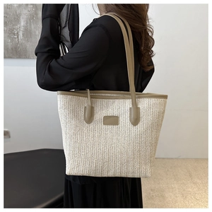 Detail of hand-woven straw tote bag featuring brown leather straps and beige woven texture