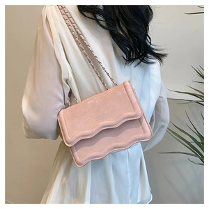 Close-up of pink suede crossbody bag featuring wavy scalloped flap and chain strap