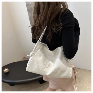 Dettaglio di una borsa tote color crema morbida con nodo decorativo indossata a spalla