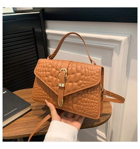 Detail of caramel brown handbag with crocodile embossed texture and gold buckle