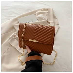 Detail of brown quilted shoulder bag featuring V-shaped stitching and gold metal accents