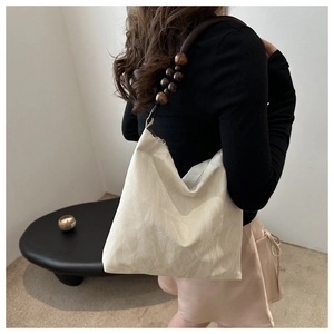 Detail of off-white pleated shoulder bag featuring distinctive brown wooden bead strap
