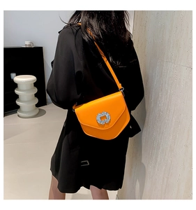 Détail d'un sac selle en cuir orange vif avec une boucle carrée sertie de diamants brillants
