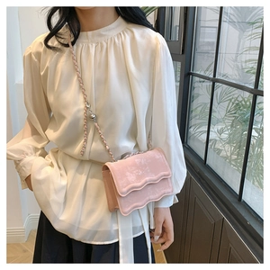 Detail of pink velvet crossbody bag with wavy flap edge and silver chain strap