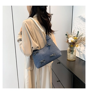 Detail of blue denim shoulder bag with decorative bows and stylish white pearl strap