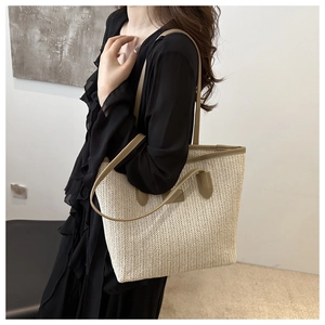 Close-up of beige straw tote bag with olive green leather handles and herringbone weave