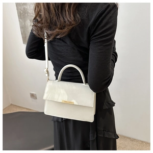 Minimalist beige structured crossbody square bag with gold metal trim shown on a model