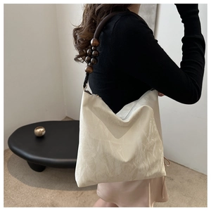Detail of beige shoulder bag featuring unique dark brown wooden bead strap design