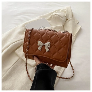 Detail of caramel quilted bag with silver bow buckle and woven chain strap