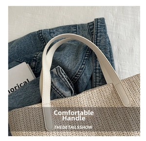 Detail of white faux leather handles stitched onto a natural woven straw tote bag