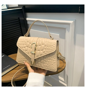 Close-up of apricot crocodile-embossed leather handbag with gold buckle on wooden table
