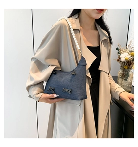 Detail of dark blue denim tote bag featuring decorative bows and white pearl shoulder strap