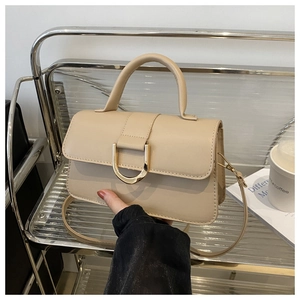 Dettaglio borsa beige con fibbia a D dorata su espositore metallico in stile moderno