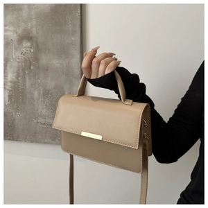 Close-up of beige leather shoulder bag with minimalist gold metal trim and flap closure