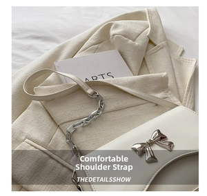 Detail of white crossbody bag featuring silver metal bow buckle and chain shoulder strap