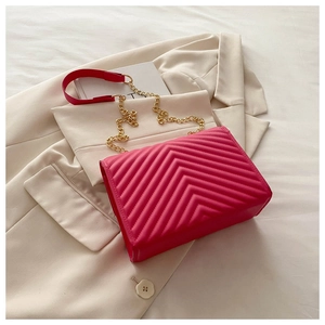Macro detail of deep pink chevron quilted leather surface and gold chain strap