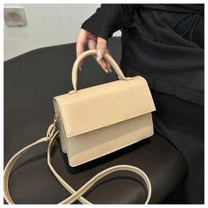 Detailed close-up of cream faux leather handbag with metal trim and detachable strap