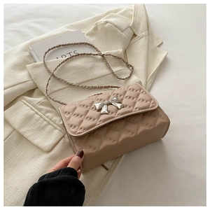 Detail of apricot quilted crossbody bag featuring silver bow buckle and chain strap