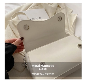 Detail view of the white crossbody bag featuring two silver hardware magnetic buckles