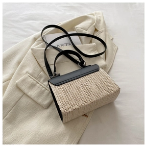 Detail of a beige woven straw bag with black leather handle on a beige blazer background