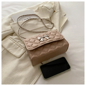 Detail of beige quilted shoulder bag featuring silver metal bow and leather chain strap