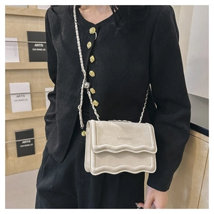 Detail of crossbody bag featuring wave edge design and metal chain strap on beige leather