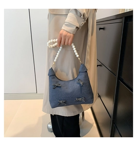 Detail of blue denim hobo bag with elegant pearl handle and stylish bow decorations