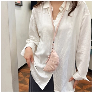 Close-up of a pink mini croissant bag with a long neck strap worn on a white shirt