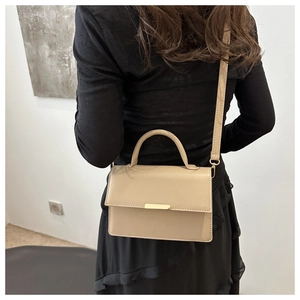 Detail view of beige crossbody bag featuring gold metal buckle clasp on model