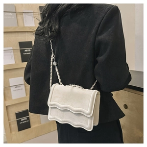 Detail of off-white crossbody bag featuring a wavy flap and silver chain with ball charm